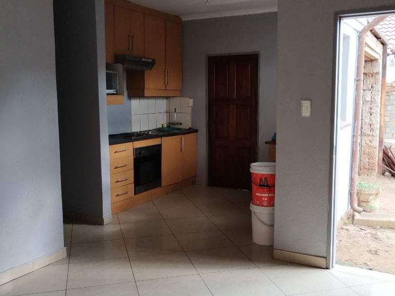 Open plan kitchen area featuring built-in cabinetry, oven, hob, and extractor fan, with neutral tiled flooring and direct access to the exterior.