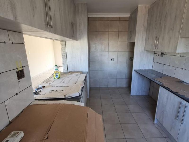 An unfinished kitchen space featuring light wood-grain cabinetry, tiled flooring, and backsplash, currently awaiting final installation and electrical finishing.