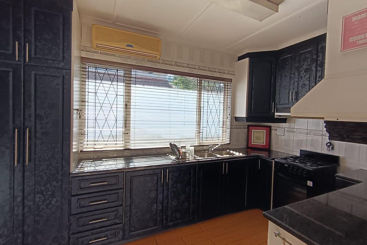 A functional kitchen featuring dark built-in cabinetry, a gas hob with extractor fan, double sink, and tiled backsplash with security bars on the window.