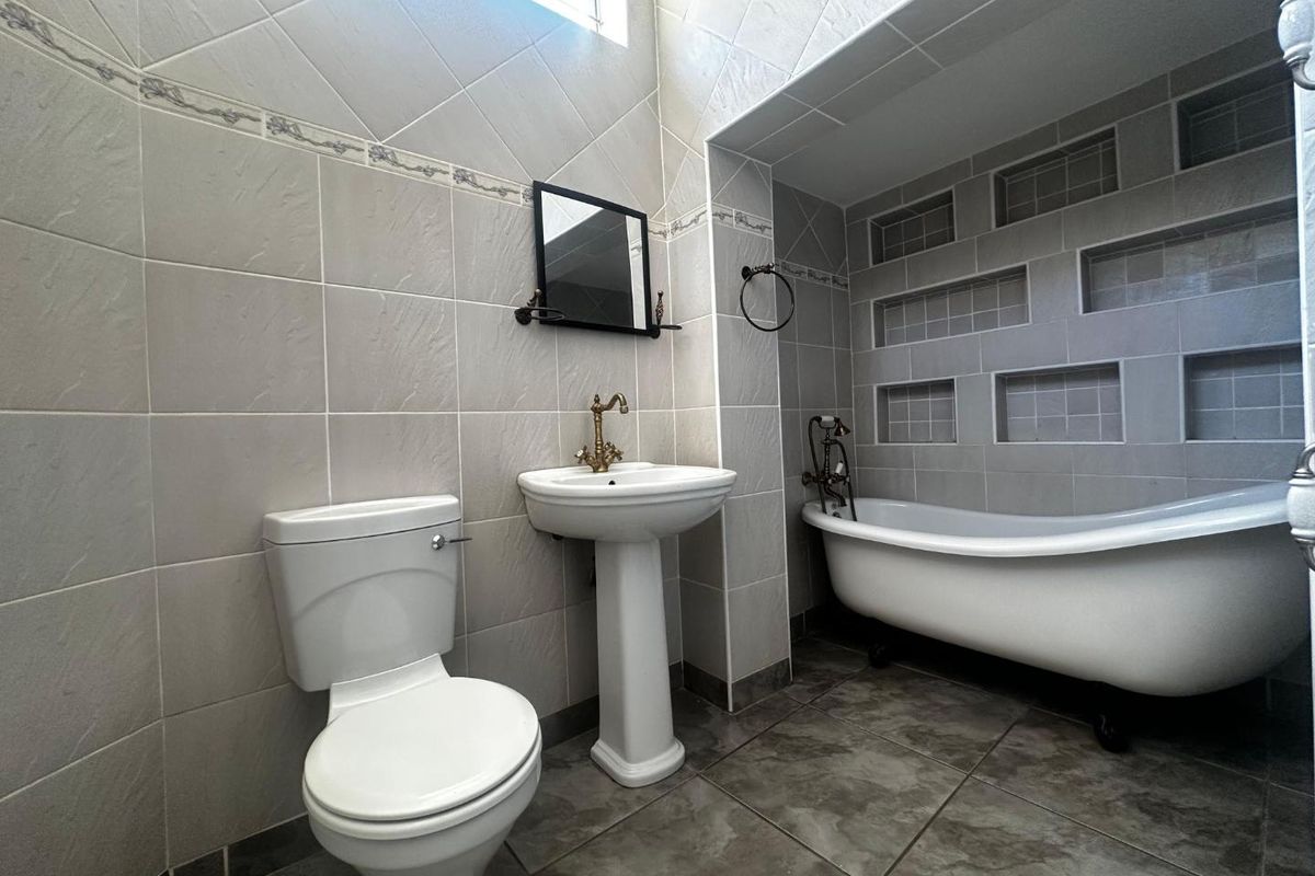 A well-maintained bathroom featuring a classic clawfoot bathtub, pedestal sink, and built-in wall niches for storage, finished with neutral ceramic tiling.