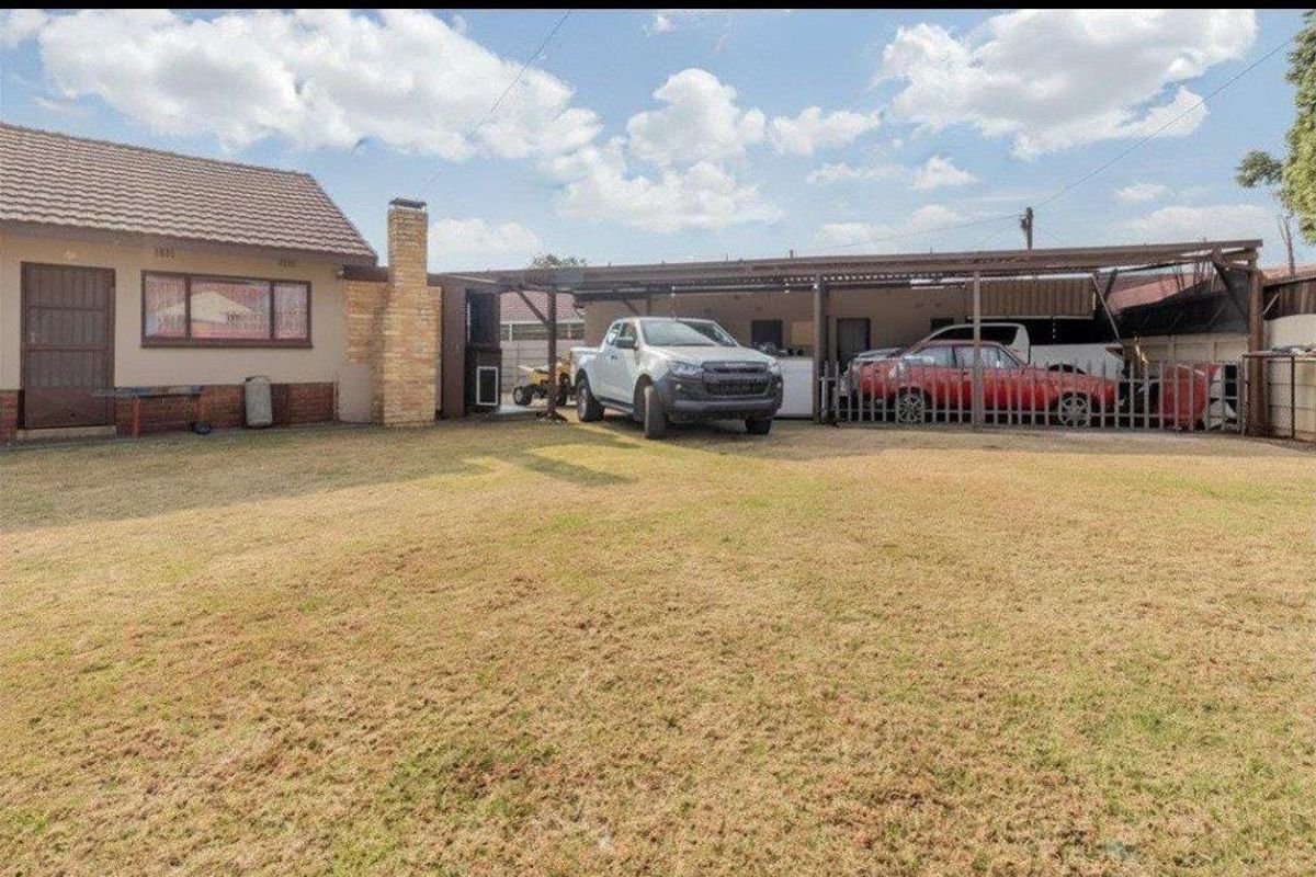 Rear view of the property featuring a large lawn, a brick chimney, and an extensive covered patio or carport area.