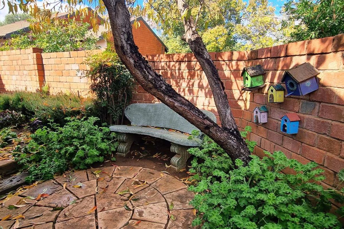 A private rear garden area featuring a circular paved patio, established trees, and a perimeter brick wall.