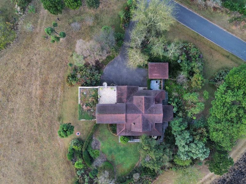Aerial view of a residential property featuring a tiled roof, paved driveway, detached garage, and established landscaped gardens on a spacious plot.