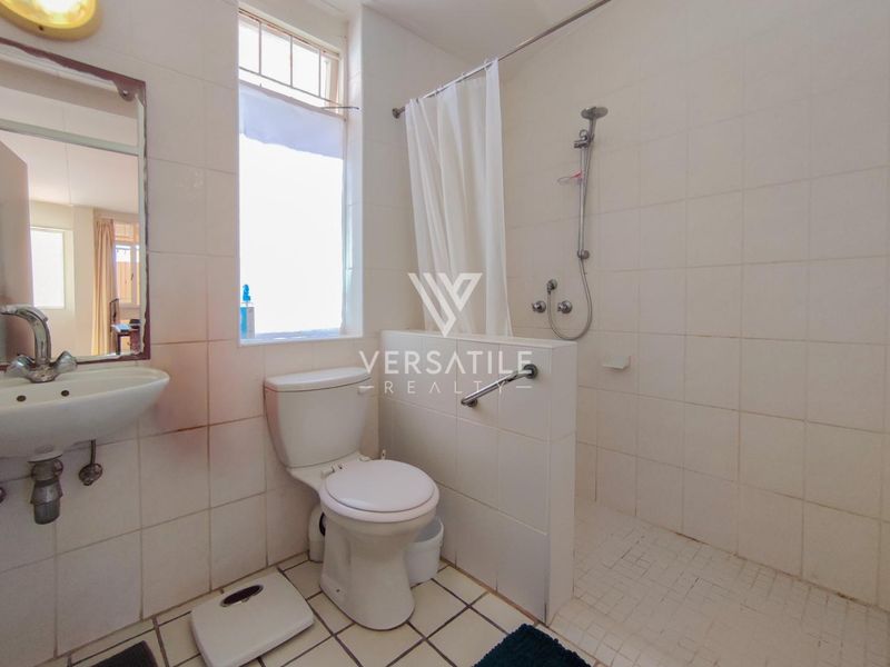 Functional bathroom featuring a wall-mounted basin, toilet, and a shower area with a safety grab rail and tiled finishes.