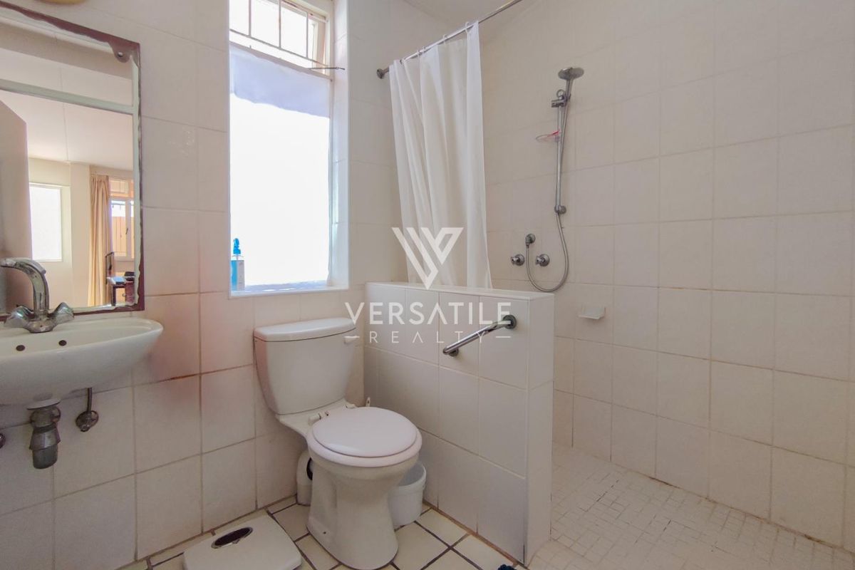 Functional bathroom featuring a wall-mounted basin, toilet, and a shower area with a safety grab rail and tiled finishes.