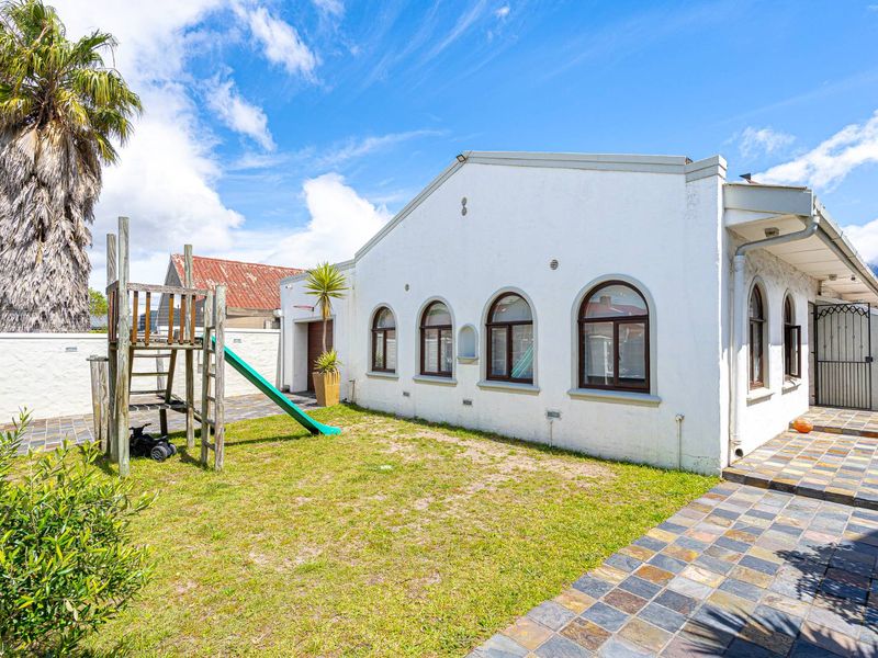 Rear exterior view of the property featuring arched windows, slate tile paving, and a private garden area with boundary wall.