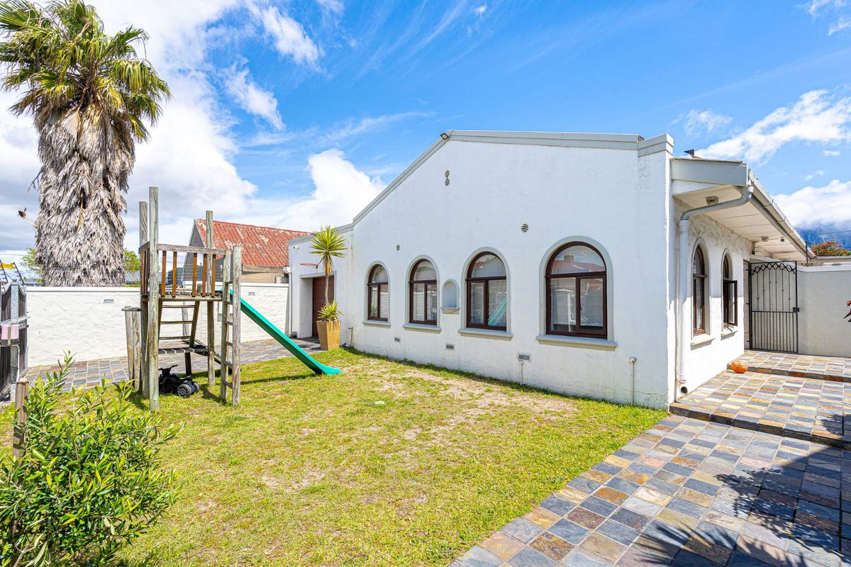 Rear exterior view of the property featuring arched windows, slate tile paving, and a private garden area with boundary wall.