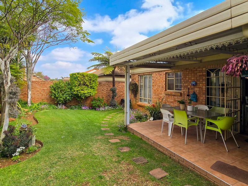 A well-maintained rear garden featuring a covered patio with tiled flooring, brick boundary walls, and a lush lawn area.