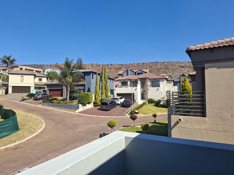 An elevated view overlooking a residential street and surrounding neighborhood with modern houses and landscaped gardens under a clear blue sky.