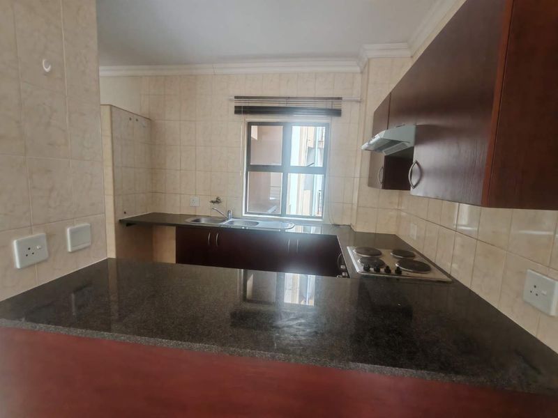 A functional kitchen featuring dark wood cabinetry, granite countertops, a breakfast bar, and a built-in electric hob with an extractor fan.