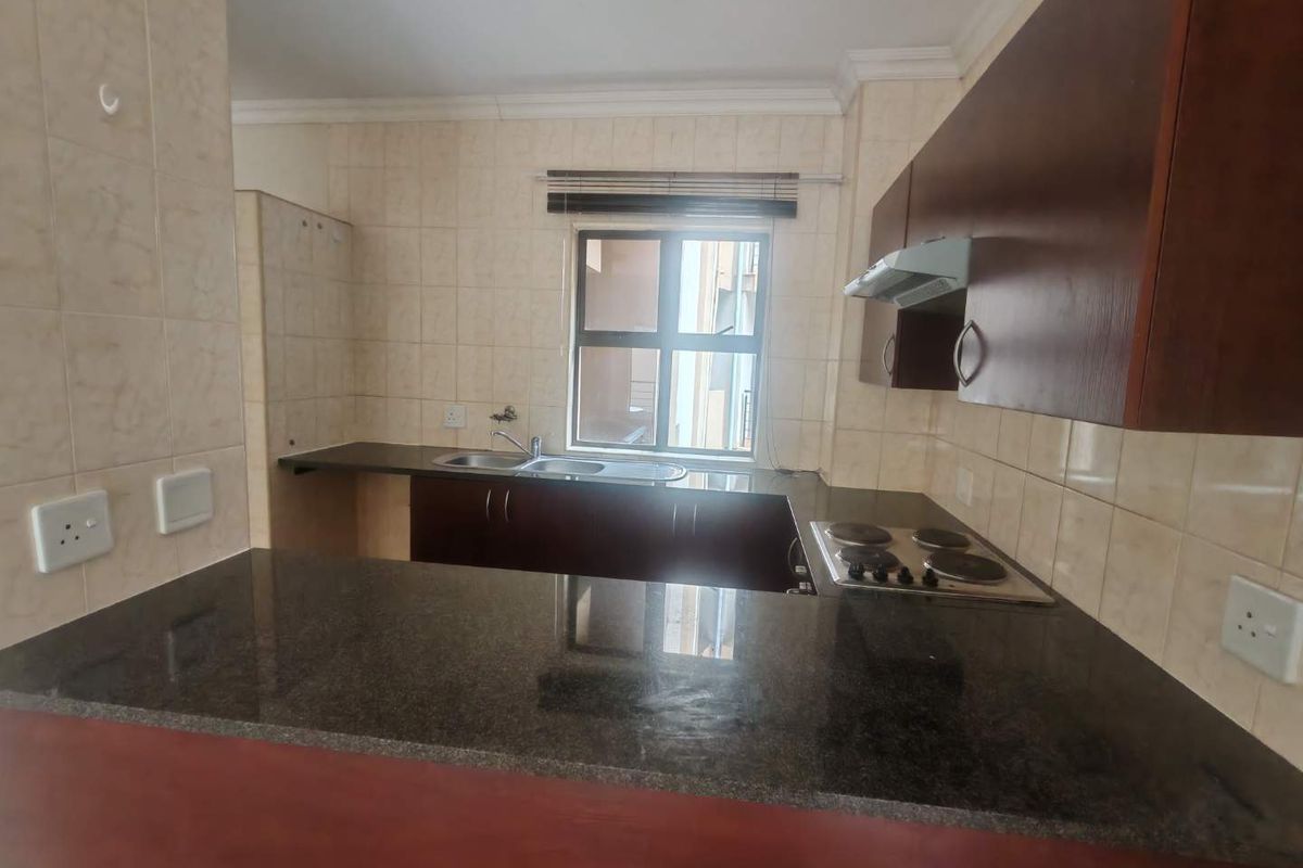 A functional kitchen featuring dark wood cabinetry, granite countertops, a breakfast bar, and a built-in electric hob with an extractor fan.
