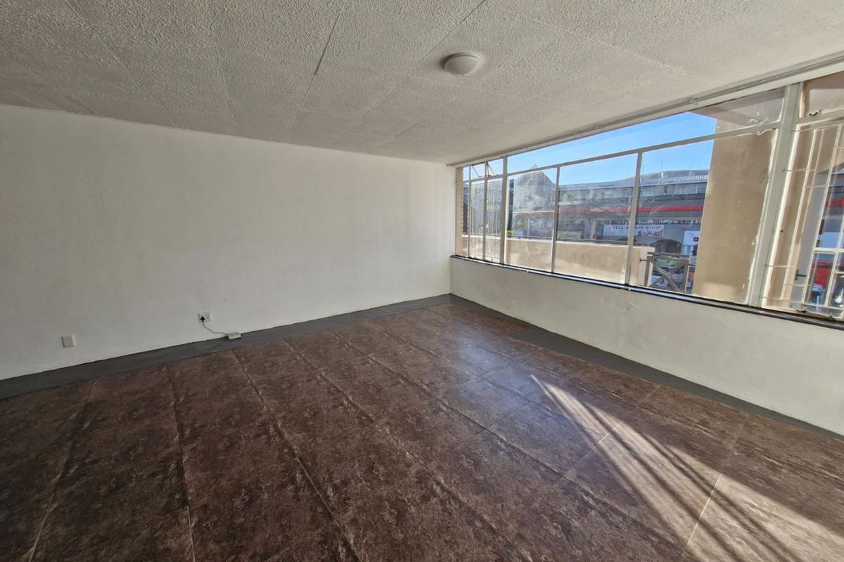 A bright, empty living area featuring large windows with security bars and dark tiled flooring, offering a blank canvas for personalization.