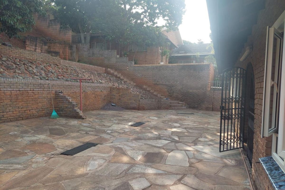 Spacious rear courtyard featuring extensive brick retaining walls, stone terracing, and paved flooring, providing a multi-level outdoor area.