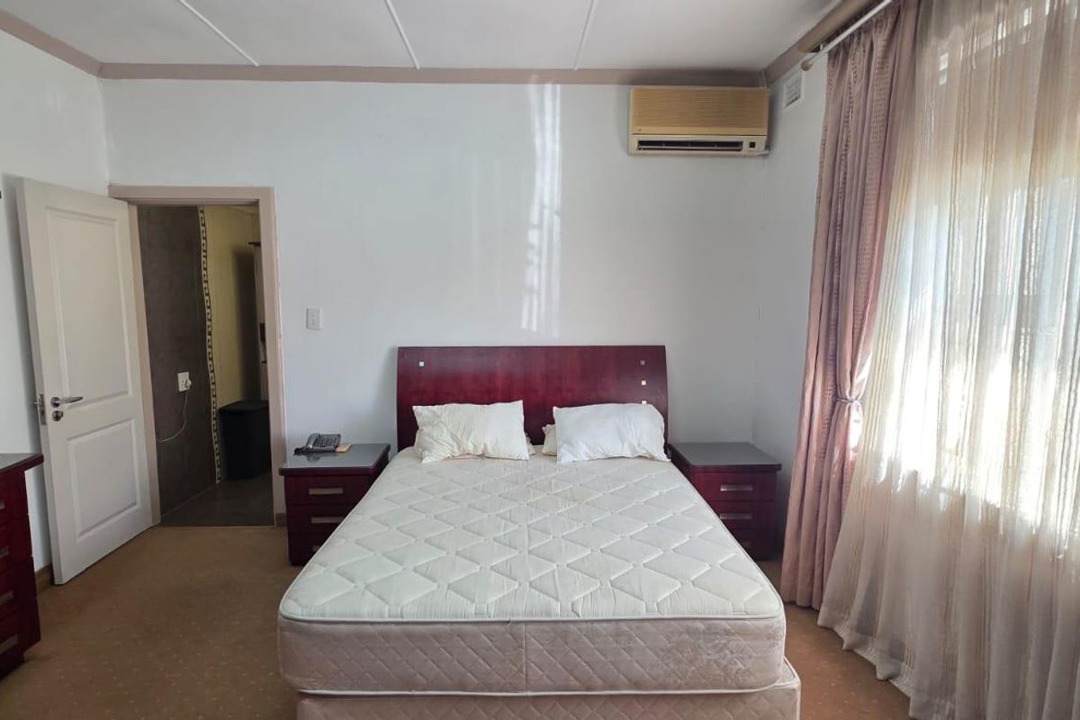 A standard bedroom featuring carpeted flooring, an integrated air conditioning unit, and direct access to an adjoining room.