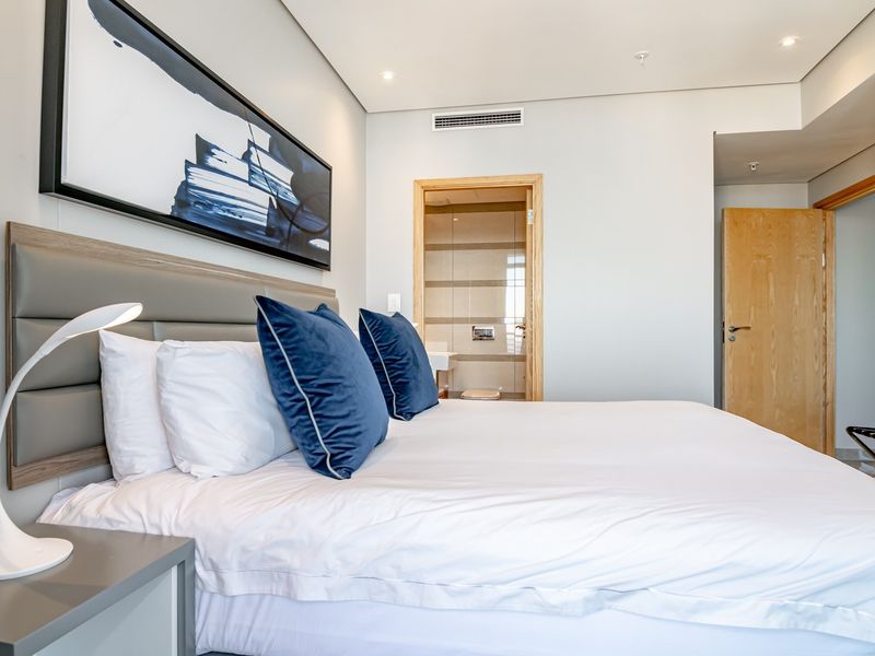 A well-maintained bedroom featuring a modern upholstered headboard, recessed lighting, ducted air conditioning, and direct access to an en-suite bathroom.