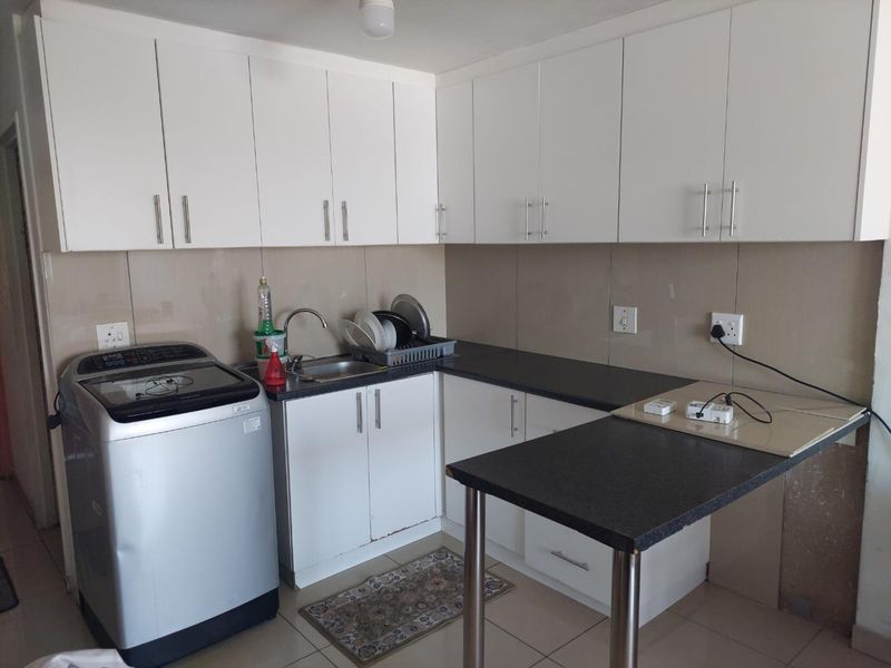 Compact kitchen featuring white cabinetry, dark countertops, a breakfast bar, and tiled splashbacks, providing a functional workspace for daily meal preparation.