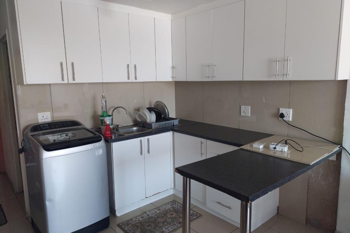 Compact kitchen featuring white cabinetry, dark countertops, a breakfast bar, and tiled splashbacks, providing a functional workspace for daily meal preparation.