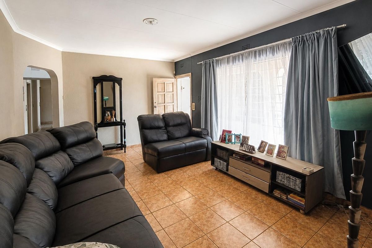 A living room featuring tiled flooring, an arched entryway, and large windows with curtain rails, providing a functional and well-lit living space.