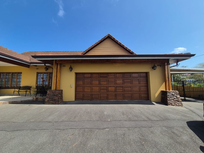 Front elevation featuring a double garage with timber door, stone-clad pillars, and timber beam accents under a tiled roof.