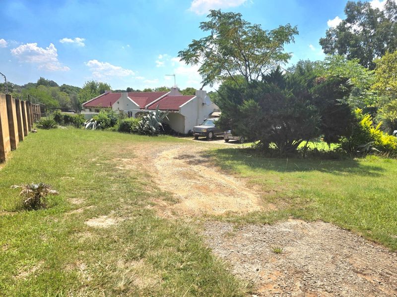 Front view of the small holding property featuring a tiled roof dwelling, perimeter walling, and a gravel driveway set within a large garden.