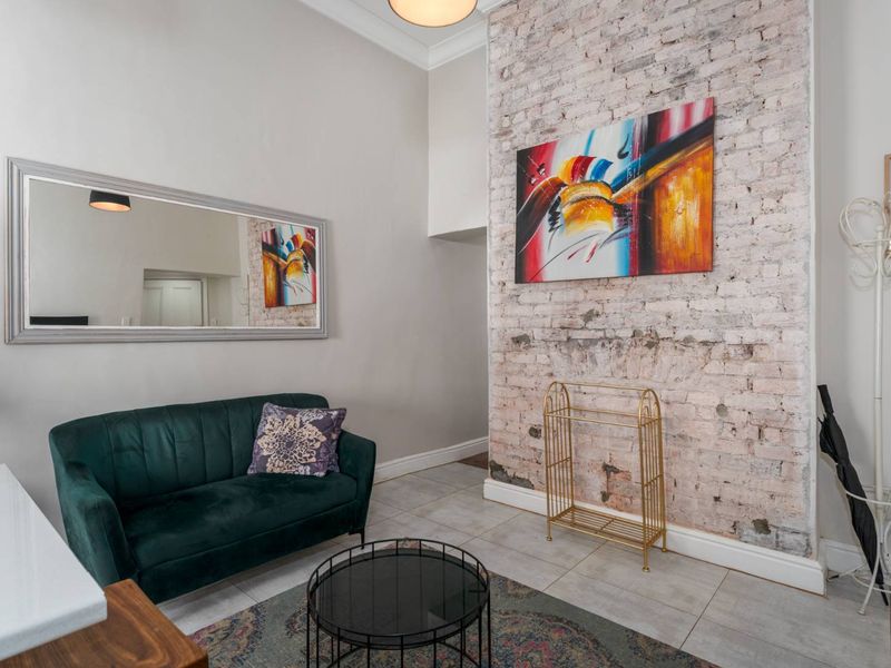 Living area featuring a prominent exposed brick feature wall, tiled flooring, and high ceilings with decorative coving.