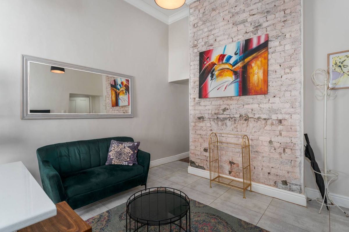 Living area featuring a prominent exposed brick feature wall, tiled flooring, and high ceilings with decorative coving.