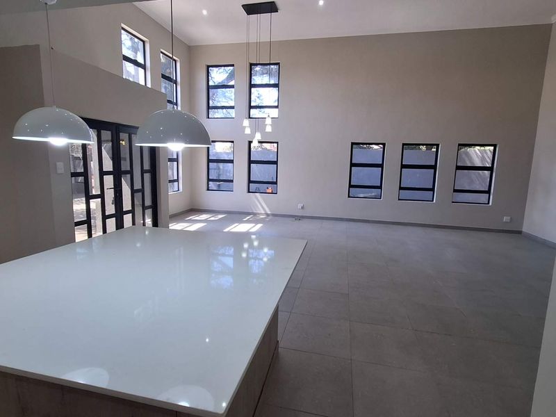 Spacious open-plan living area featuring large windows, modern tiled flooring, and a central kitchen island with pendant lighting.