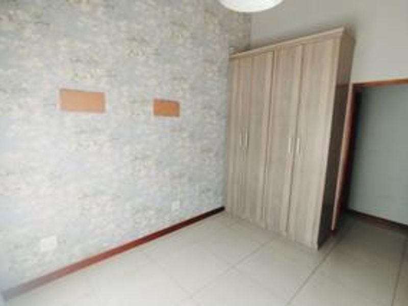 A bright, empty bedroom featuring tiled flooring, a built-in wardrobe, and decorative wallpaper, offering a clean canvas for personalization.