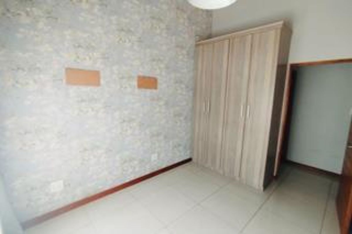 A bright, empty bedroom featuring tiled flooring, a built-in wardrobe, and decorative wallpaper, offering a clean canvas for personalization.