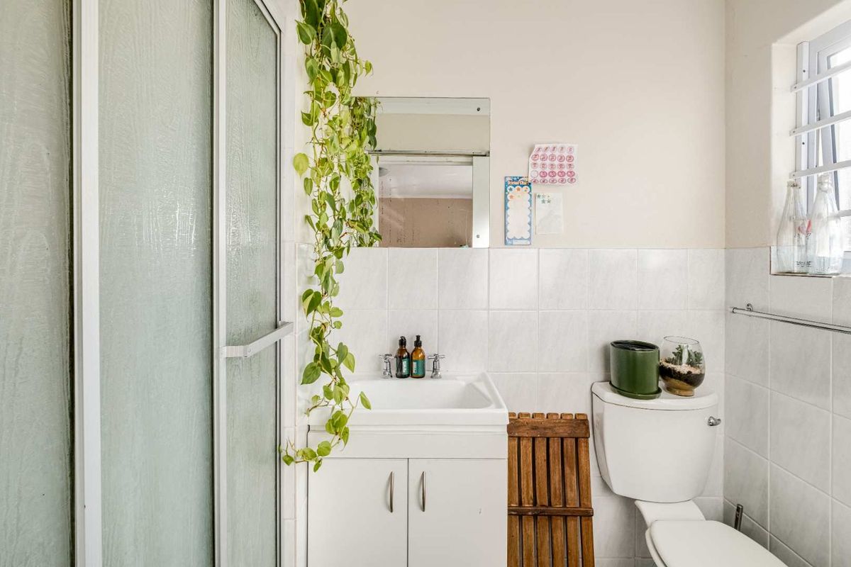 A functional bathroom featuring a shower enclosure, a vanity basin with storage, and a standard toilet, finished with white wall tiling.