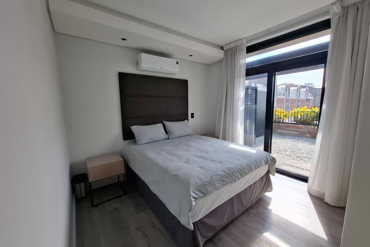 Modern bedroom featuring laminate flooring, a wall-mounted air conditioning unit, and large sliding glass doors providing access to an outdoor patio area.