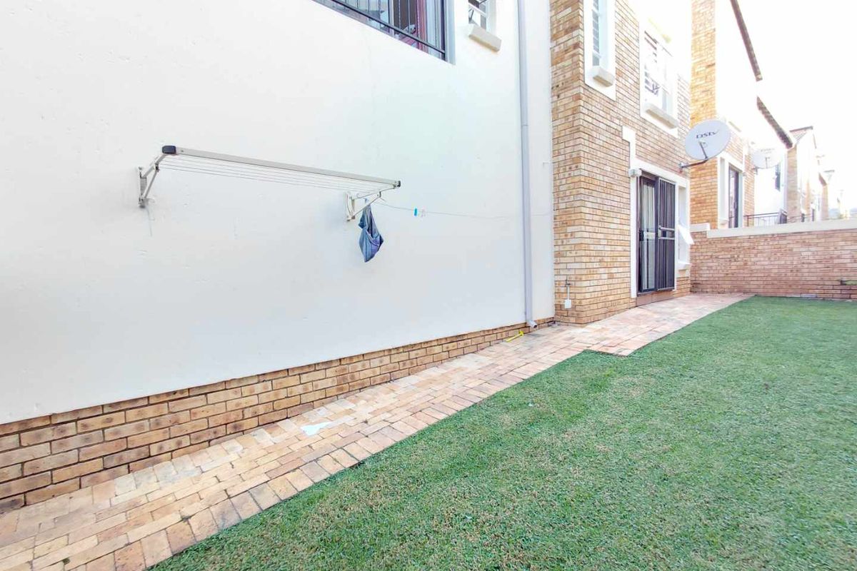 A private rear garden area featuring a paved walkway, brick facade detailing, and a wall-mounted retractable washing line.