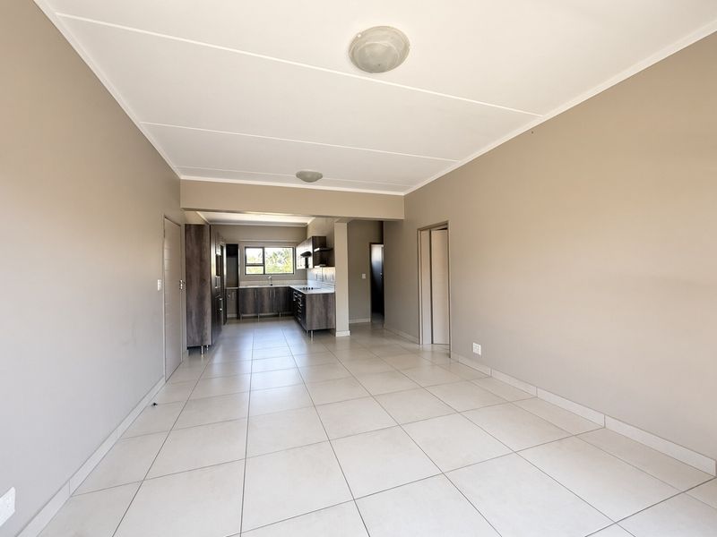 An open-plan living and kitchen area featuring neutral wall tones, tiled flooring, and modern built-in cabinetry with integrated kitchen appliances.