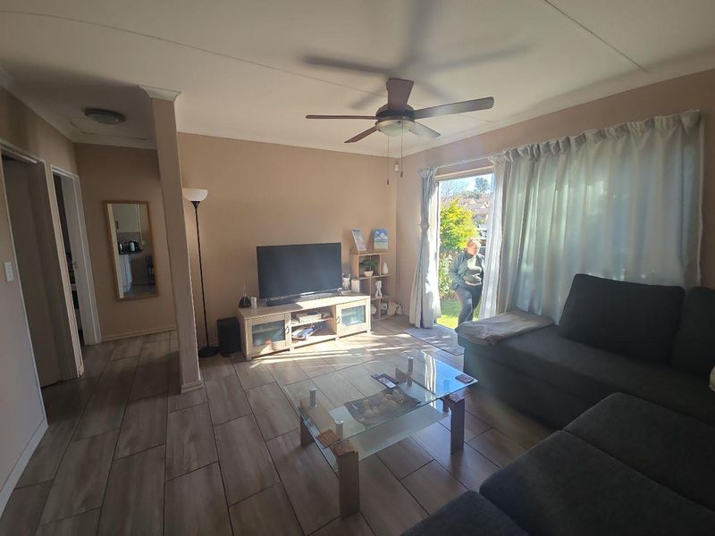 A living room featuring tiled flooring, a ceiling fan, and a sliding glass door providing access to the outdoor area.