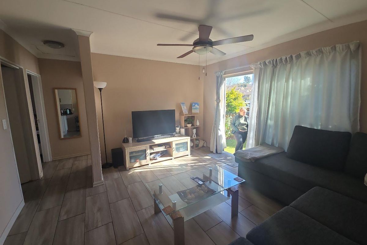 A living room featuring tiled flooring, a ceiling fan, and a sliding glass door providing access to the outdoor area.