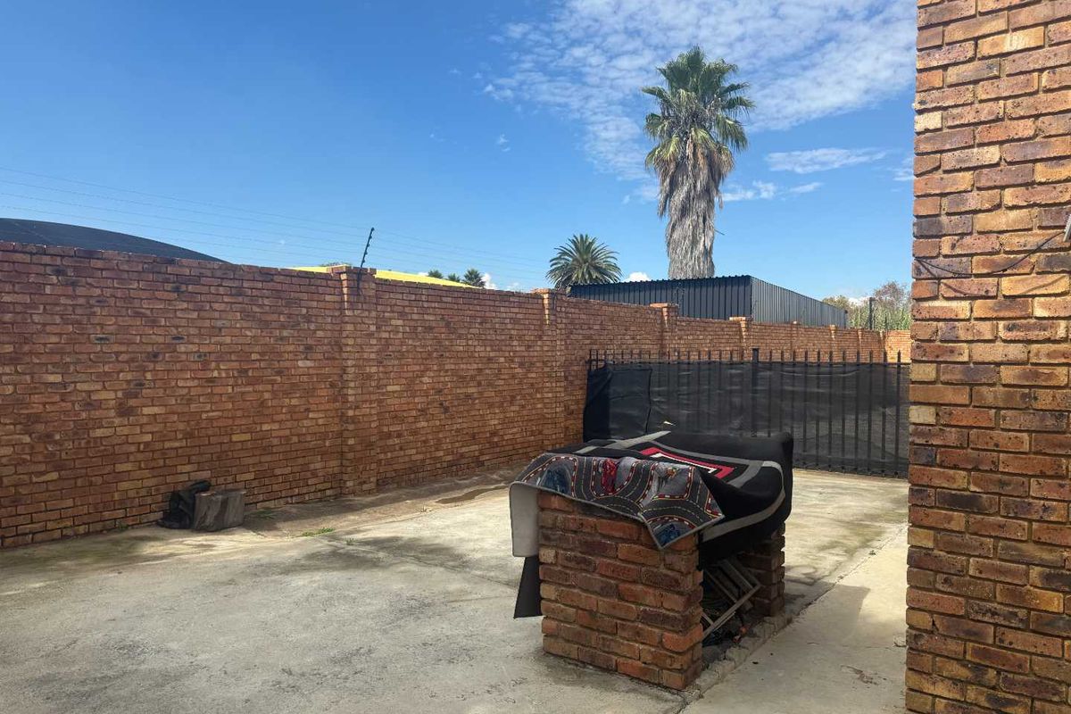 A private rear courtyard featuring a built-in brick braai area, enclosed by high perimeter brick walls and security fencing.
