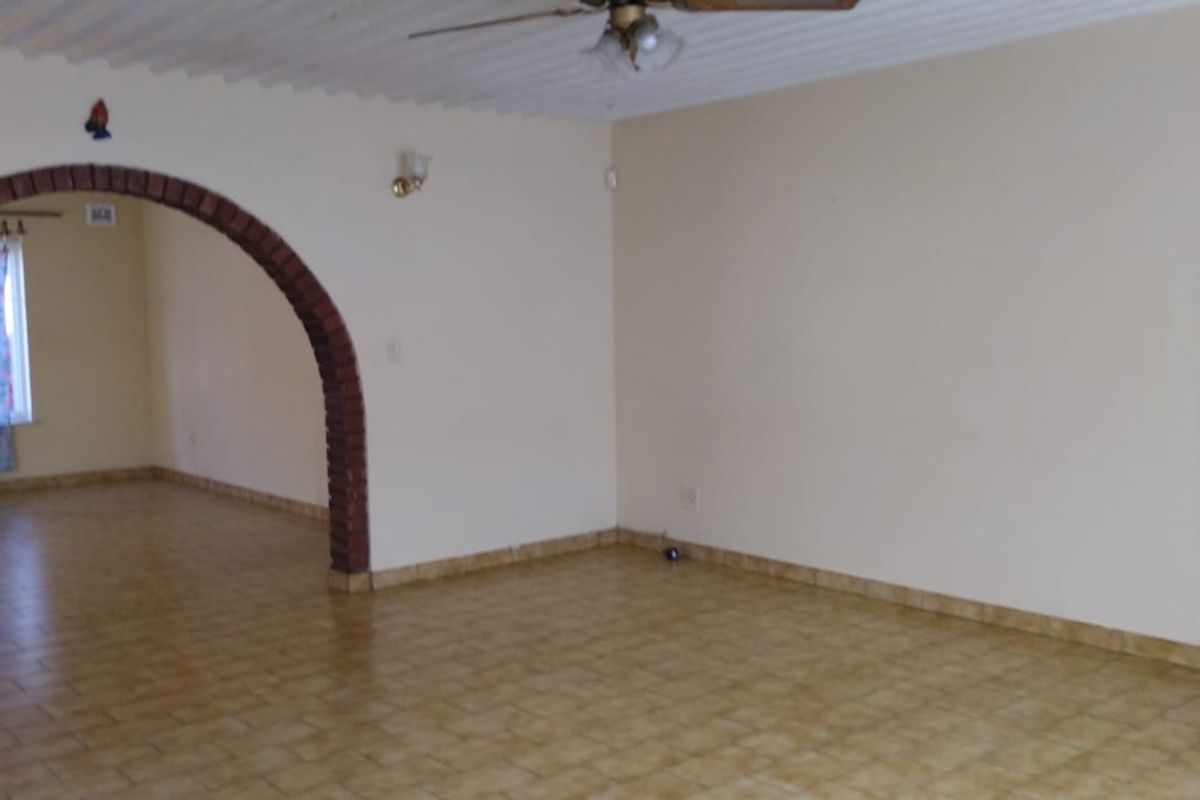 Spacious living area featuring a distinctive brick archway, tiled flooring, and a ceiling fan, offering a versatile layout for comfortable family living.