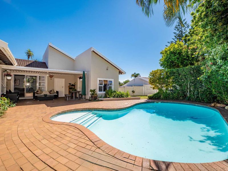 A well-maintained outdoor entertainment area featuring a swimming pool, brick-paved patio, and a covered terrace attached to the main residence.