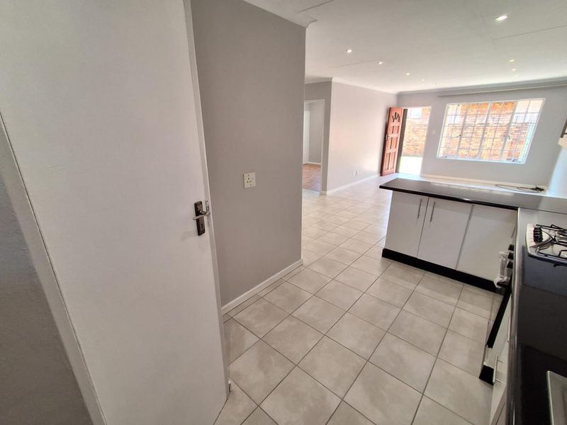 An open-plan living and kitchen area featuring neutral tiled flooring, recessed lighting, and a functional kitchen layout with built-in cabinetry and a breakfast bar.