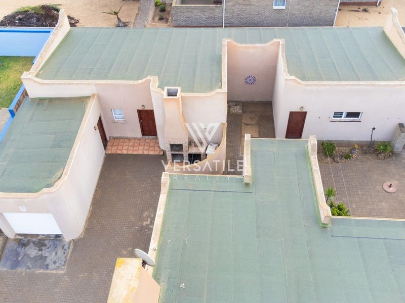 Aerial view of the property showing the paved courtyard, built-in braai area, garage, and flat roof structure.