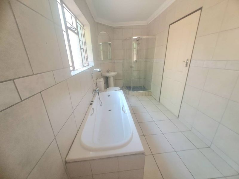 A functional bathroom featuring a built-in bathtub, corner shower enclosure, pedestal basin, and toilet, finished with neutral wall and floor tiling.
