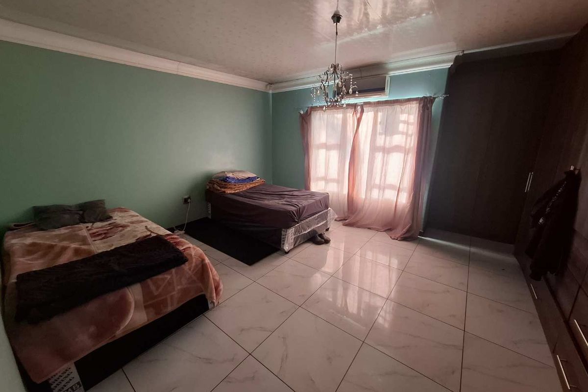 Spacious bedroom featuring large format floor tiles, built-in cupboards, and a wall-mounted air conditioning unit.