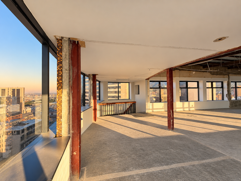 Spacious open-plan penthouse area featuring floor-to-ceiling windows with city views, exposed structural steel columns, and an unfinished interior ready for custom renovation.