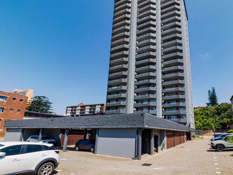 Exterior view of a multi-story apartment building featuring a paved driveway and covered parking bays.