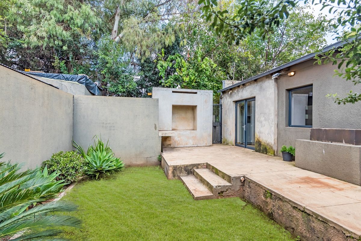 Rear courtyard featuring a concrete patio, built-in braai area, and small lawn, requiring some maintenance to the exterior finishes.