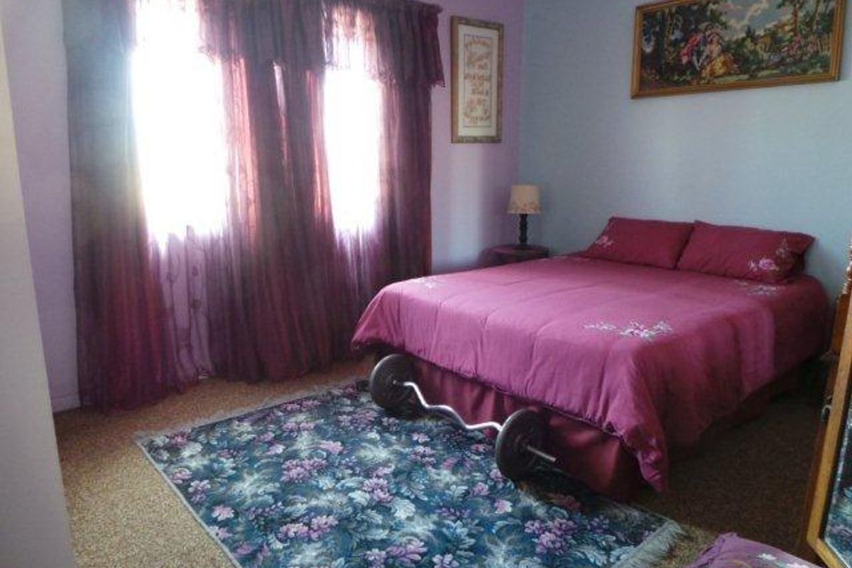 A bedroom featuring carpeted flooring and large windows with curtains, providing a functional space for rest.