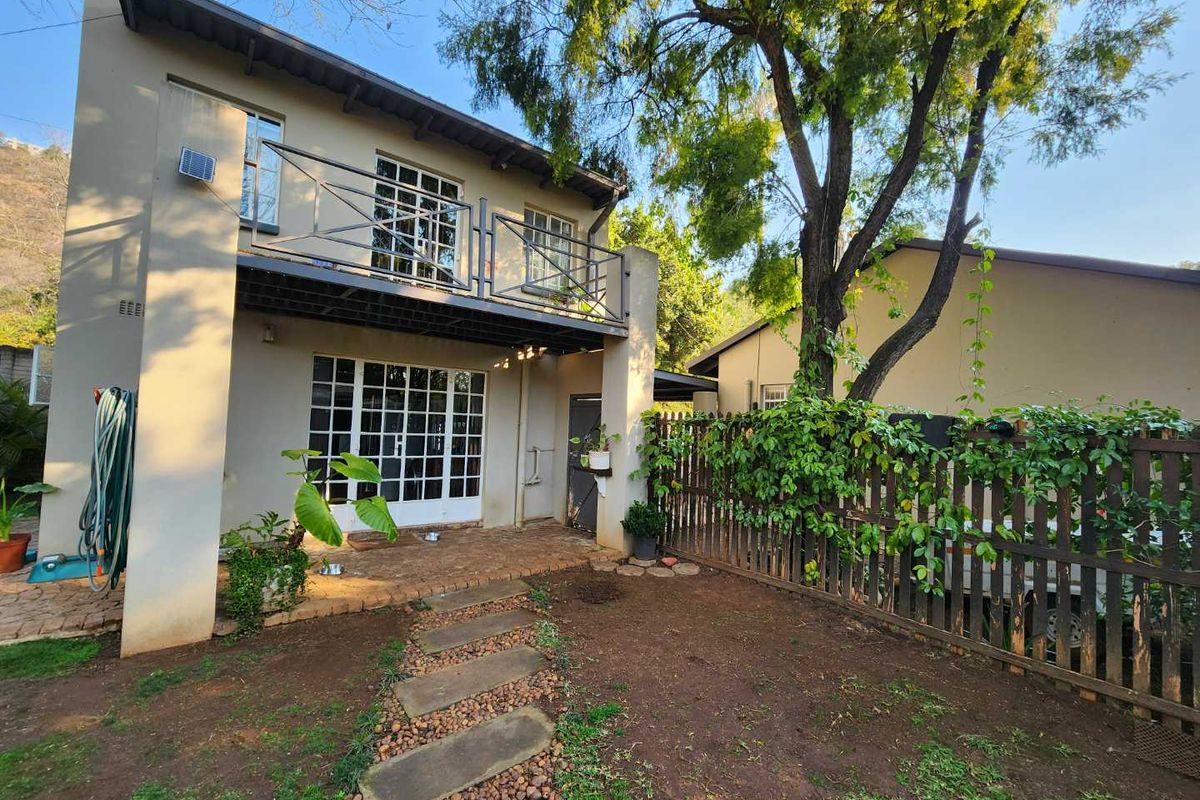 Rear exterior view featuring a brick patio, stone pathway, and a second-story balcony with metal railings overlooking a garden area.