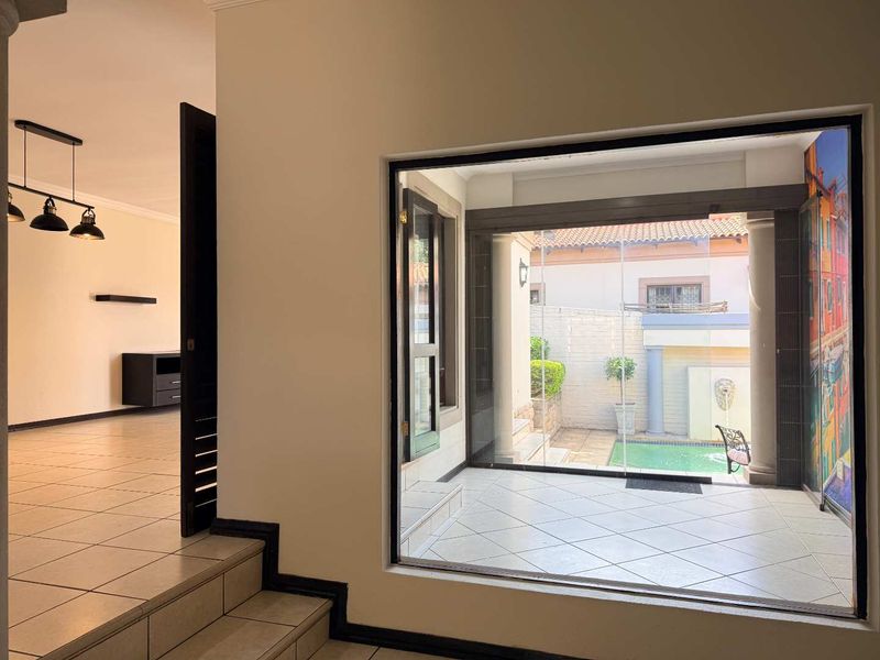 Spacious living area featuring tiled floors, modern pendant lighting, and a large picture window overlooking a private patio and pool area.