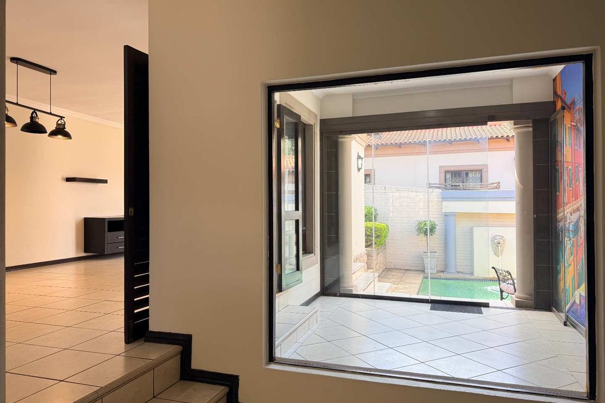 Spacious living area featuring tiled floors, modern pendant lighting, and a large picture window overlooking a private patio and pool area.