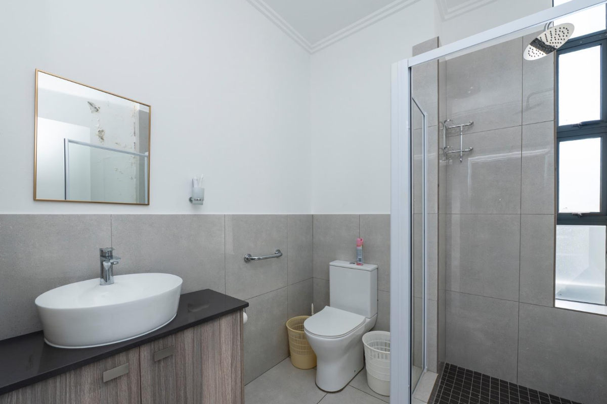 Modern bathroom featuring a vessel sink on a vanity cabinet, a toilet, and a glass-enclosed shower with grey wall tiles.